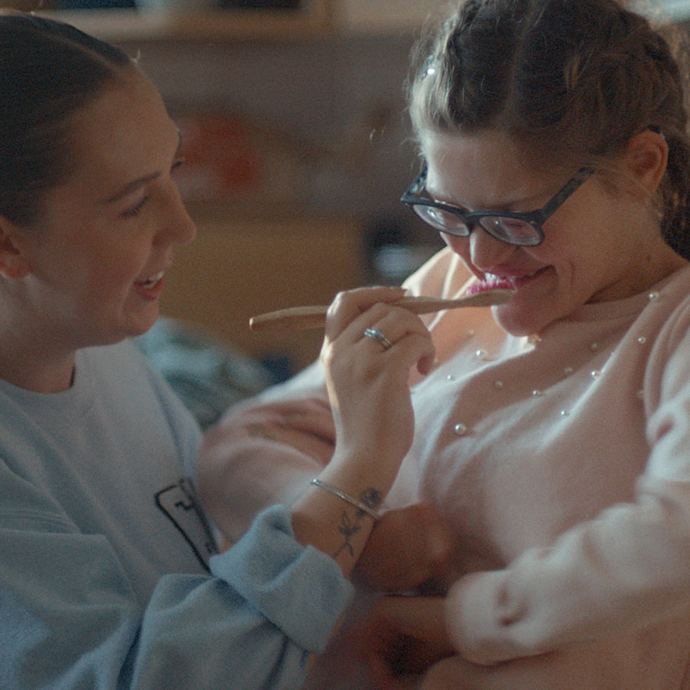 A smiling young woman helps her laughing teenage sister brush her teeth. A smiling young woman helps her laughing teenage sister brush her teeth.